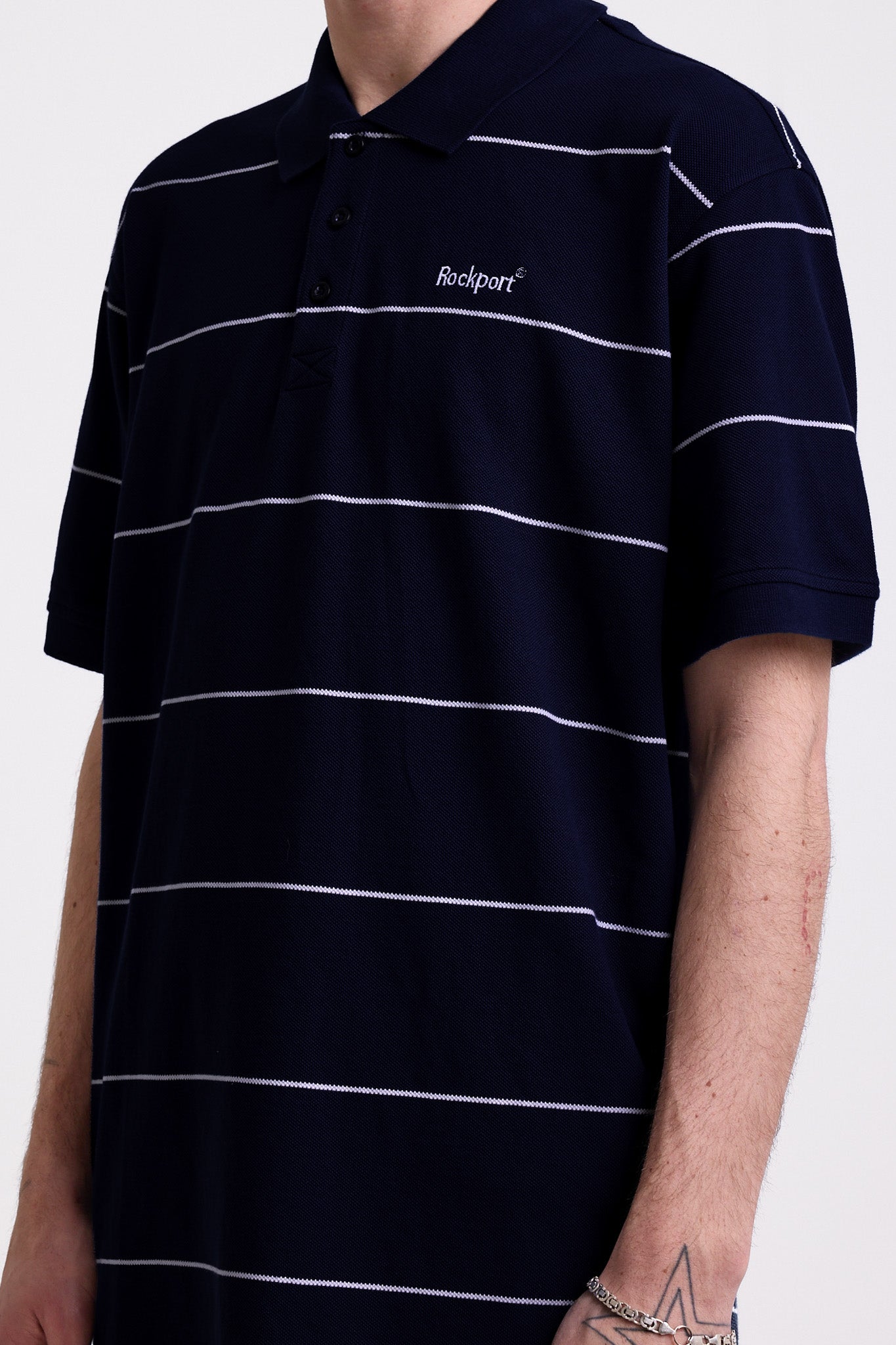 Navy and white striped pique polo shirt with embroidered Rockport logo, worn by model