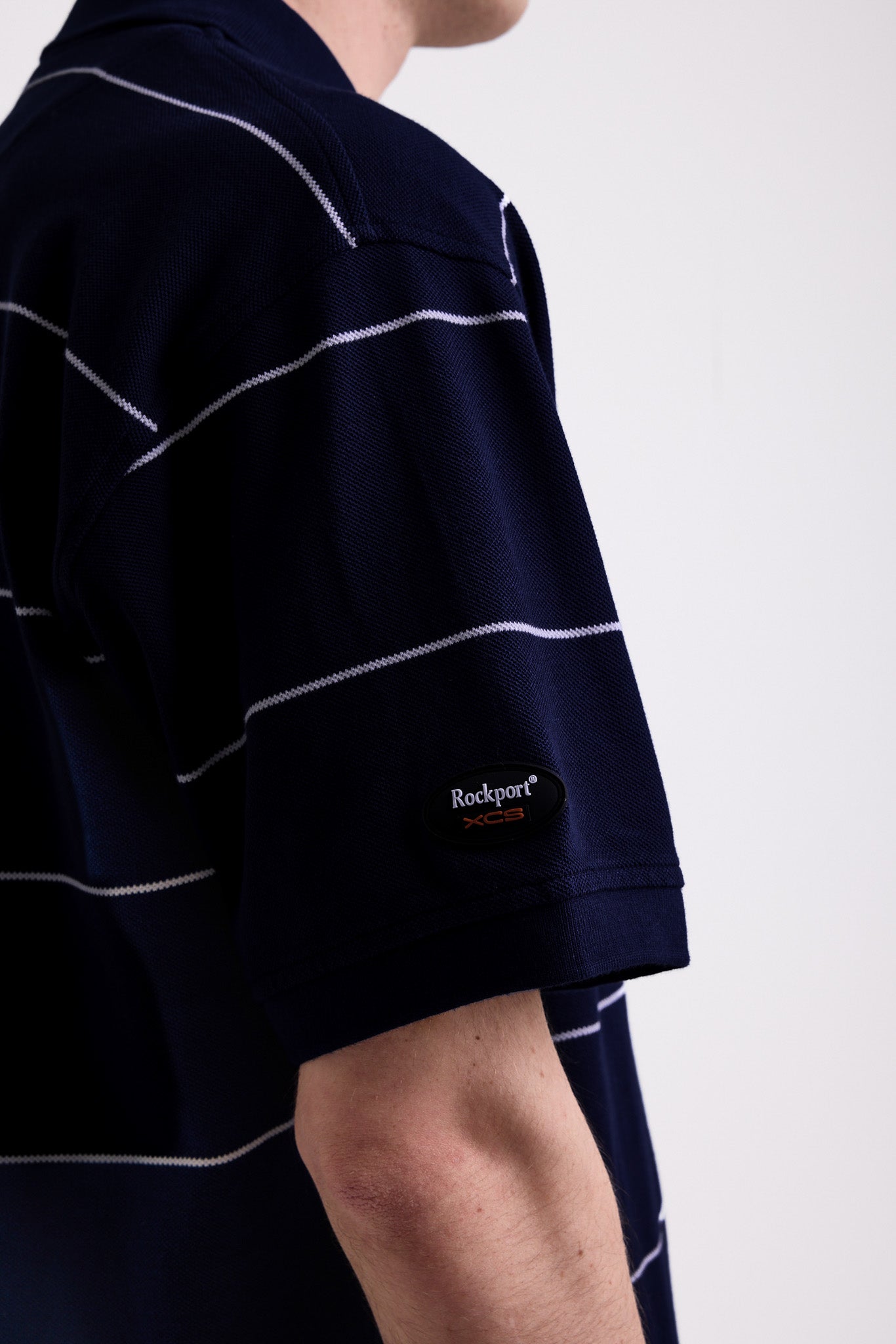Navy and white striped pique polo shirt with embroidered Rockport logo, worn by model