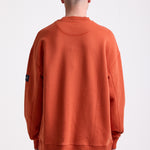 Burnt orange cotton crew neck sweatshirt with embroidered Rockport logo and american flag at chest, worn by model