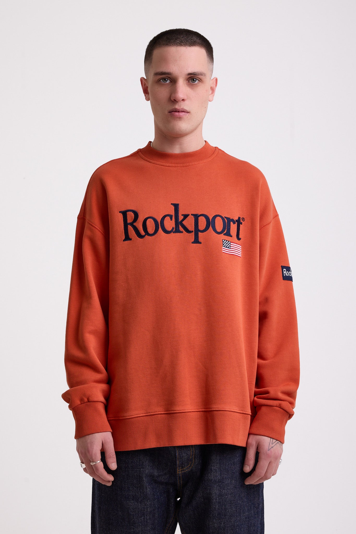 Burnt orange cotton crew neck sweatshirt with embroidered Rockport logo and american flag at chest, worn by model