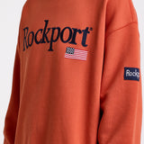 Burnt orange cotton crew neck sweatshirt with embroidered Rockport logo and american flag at chest, worn by model