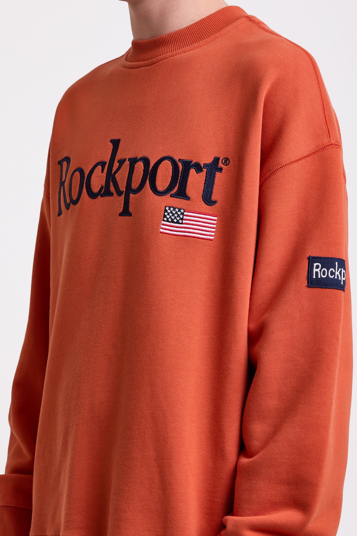 Burnt orange cotton crew neck sweatshirt with embroidered Rockport logo and american flag at chest, worn by model
