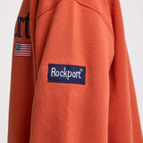 Burnt orange cotton crew neck sweatshirt with embroidered Rockport logo and american flag at chest, worn by model