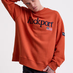 Burnt orange cotton crew neck sweatshirt with embroidered Rockport logo and american flag at chest, worn by model