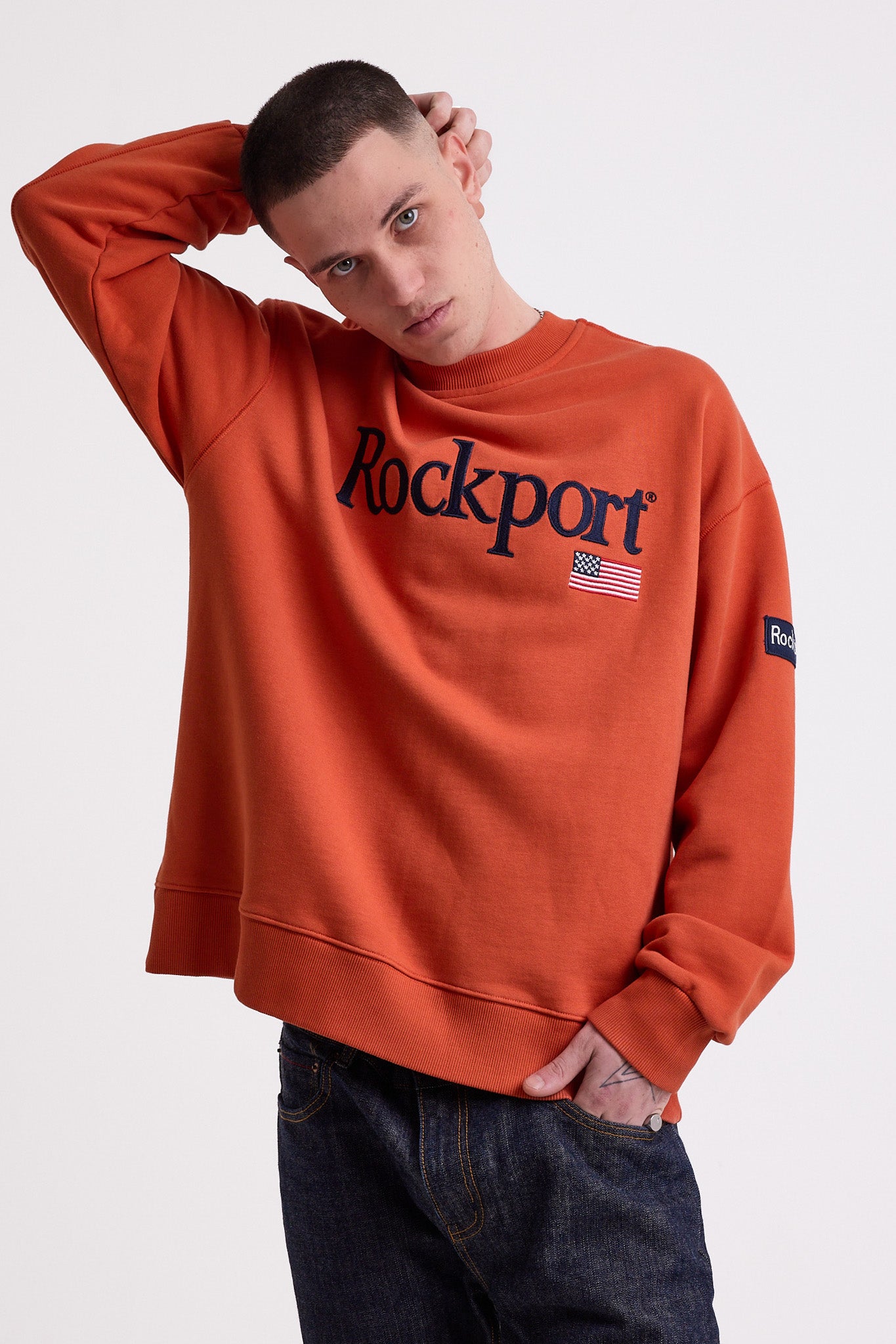 Burnt orange cotton crew neck sweatshirt with embroidered Rockport logo and american flag at chest, worn by model