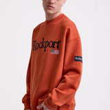 Burnt orange cotton crew neck sweatshirt with embroidered Rockport logo and american flag at chest, worn by model