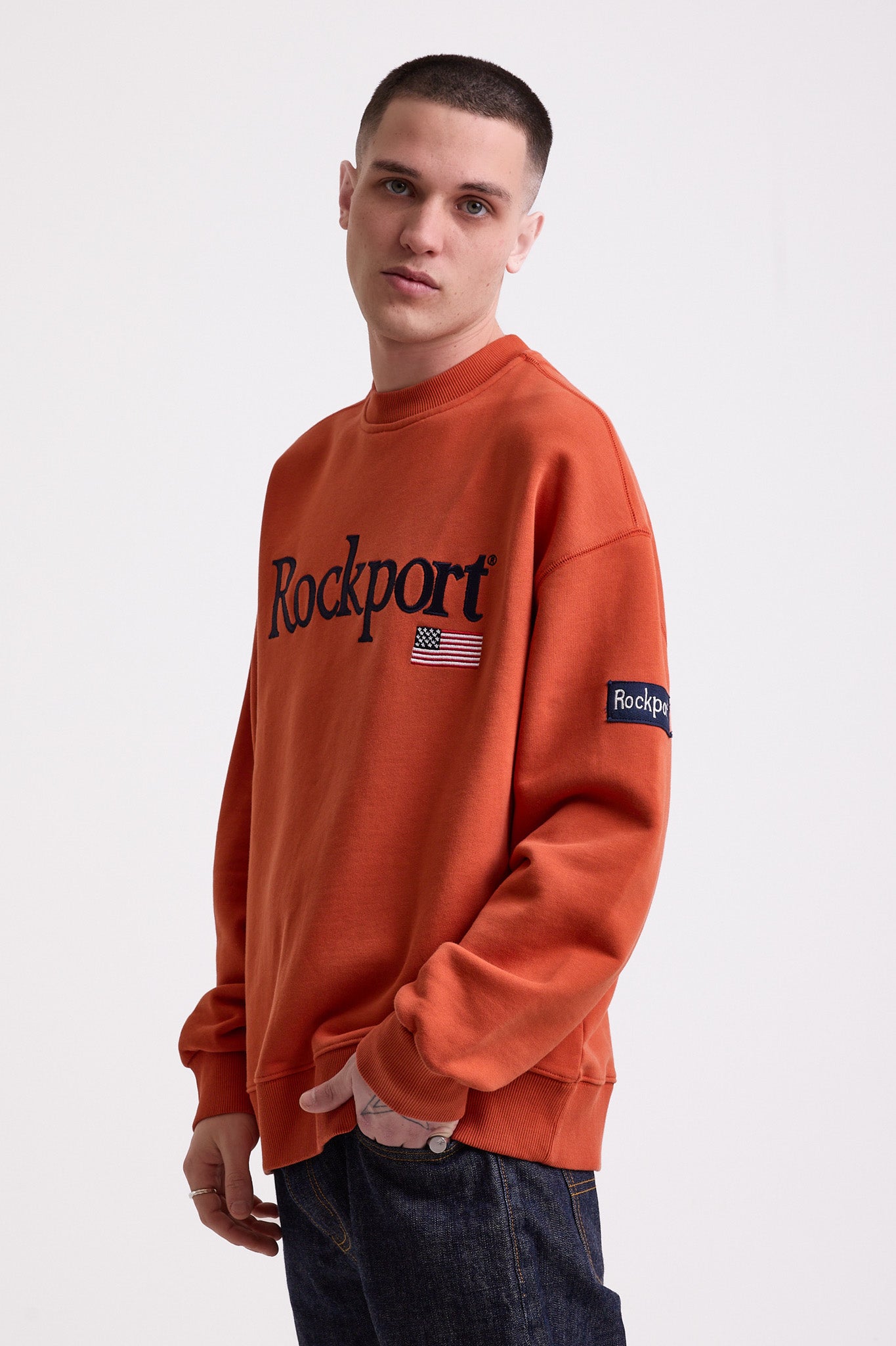 Burnt orange cotton crew neck sweatshirt with embroidered Rockport logo and american flag at chest, worn by model