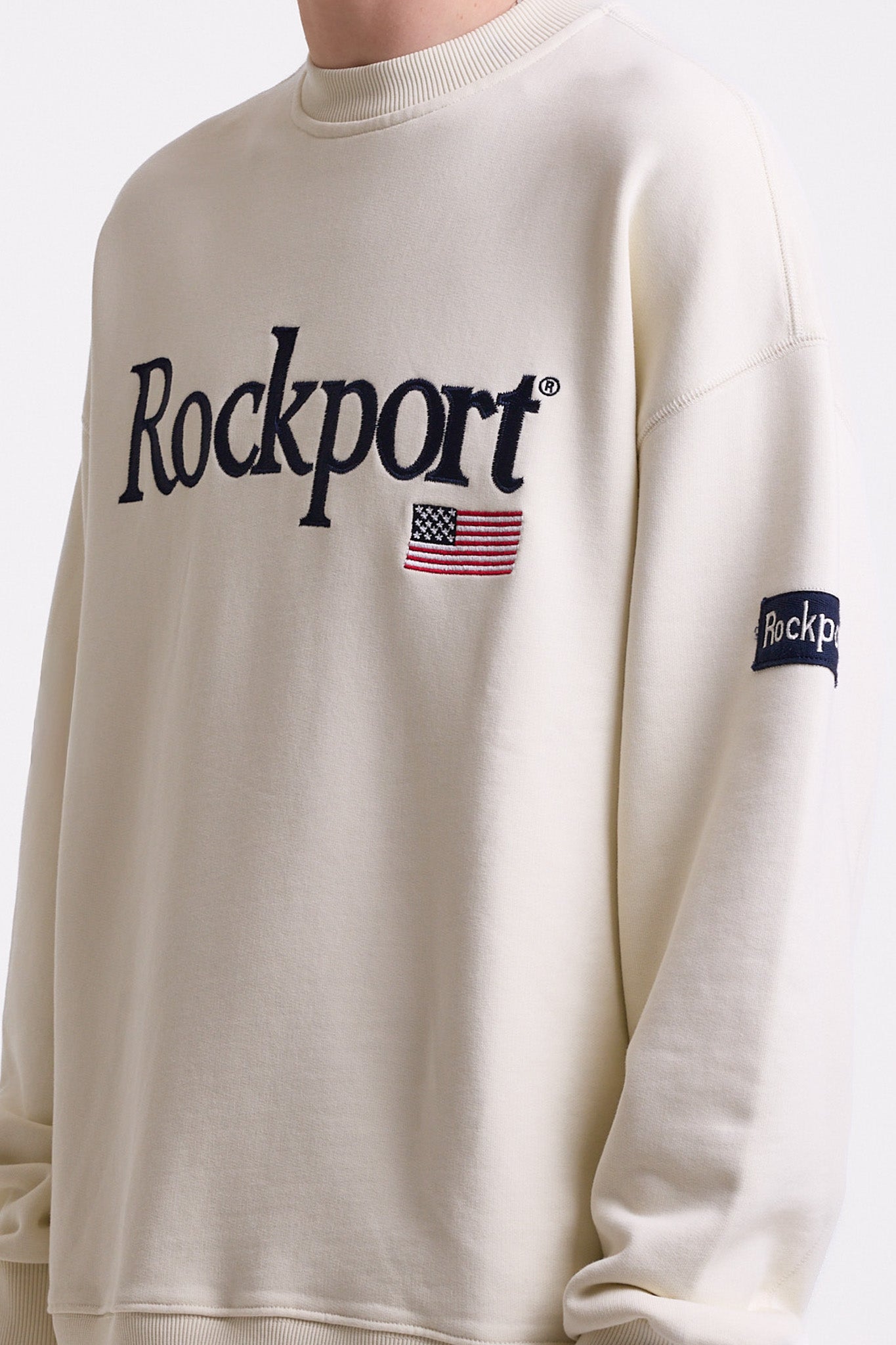 Ecru cotton crew neck sweatshirt with embroidered Rockport logo and american flag at chest, worn by model